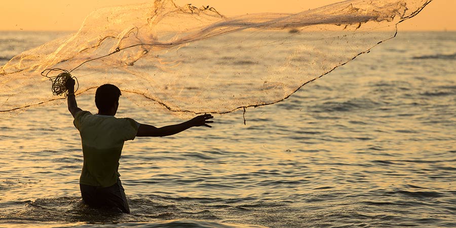 A fisherman throws his net in the ocean.